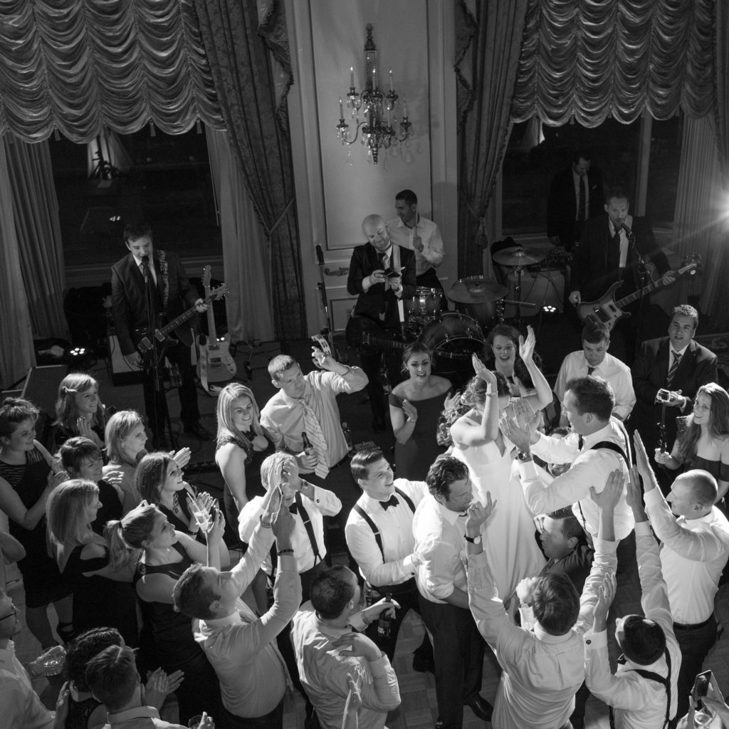 black and white image of bride and groom on crowd's shoulders in ballroom from above